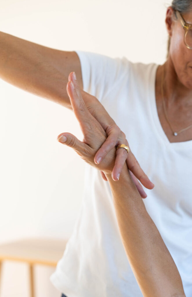 Das Bild zeigt den kinesiologischen Muskeltest. Eine Frau übt mit der Hand leichten Druck auf den ausgestreckten Arm einer zweiten Person aus.