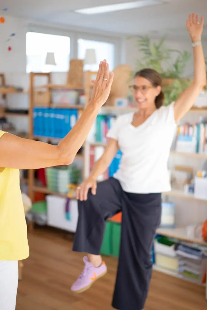 Zwei Frauen führen eine Balance-Übung auf einem Bein aus.