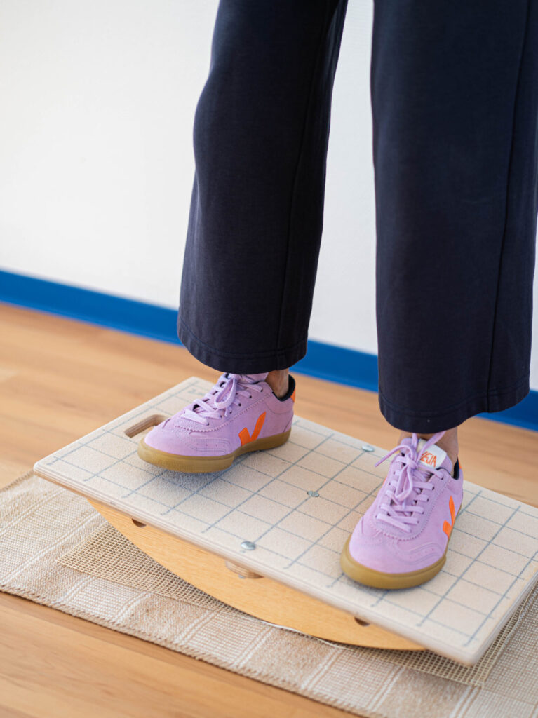 Das Bild zeigt eine Person von den Knien abwärts. Sie balanciert auf einem Holzbrett.