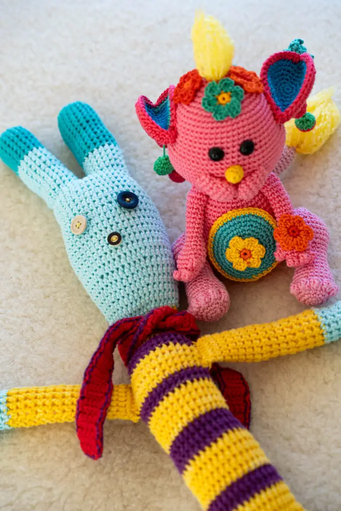 Zwei bunte, gehäkelte Kuscheltiere.